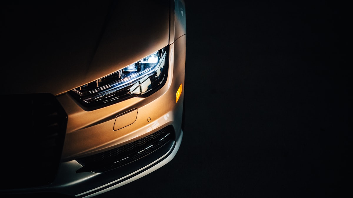 Headlight and front fender of a modern car lit amber against a black background
